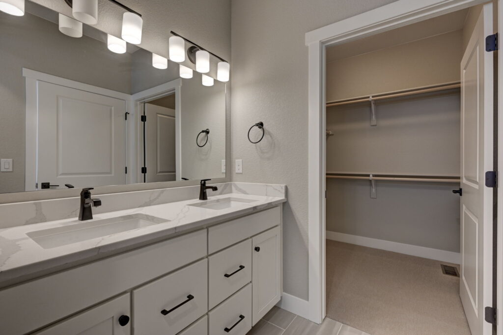 Double-sink vanity beside an open walk-in closet doorway, large mirror overhead.