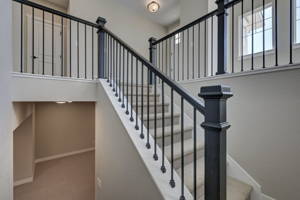 Carpeted staircase with black metal balusters and dark-stained handrail opening to an upper landing.