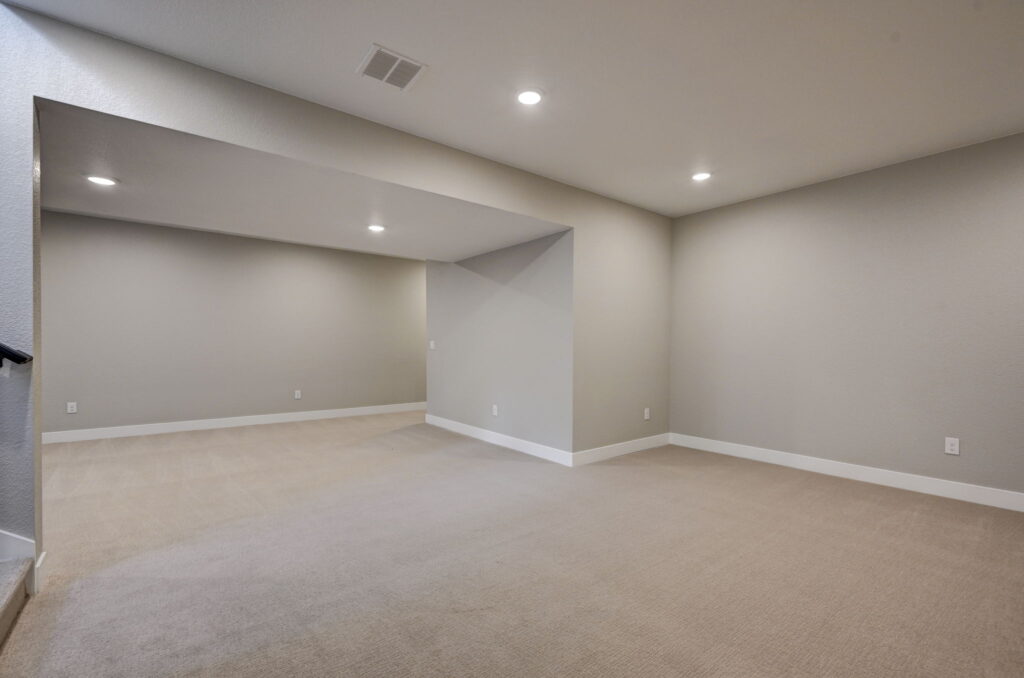 Large empty carpeted room with recessed lighting and a recessed alcove area under a low ceiling.