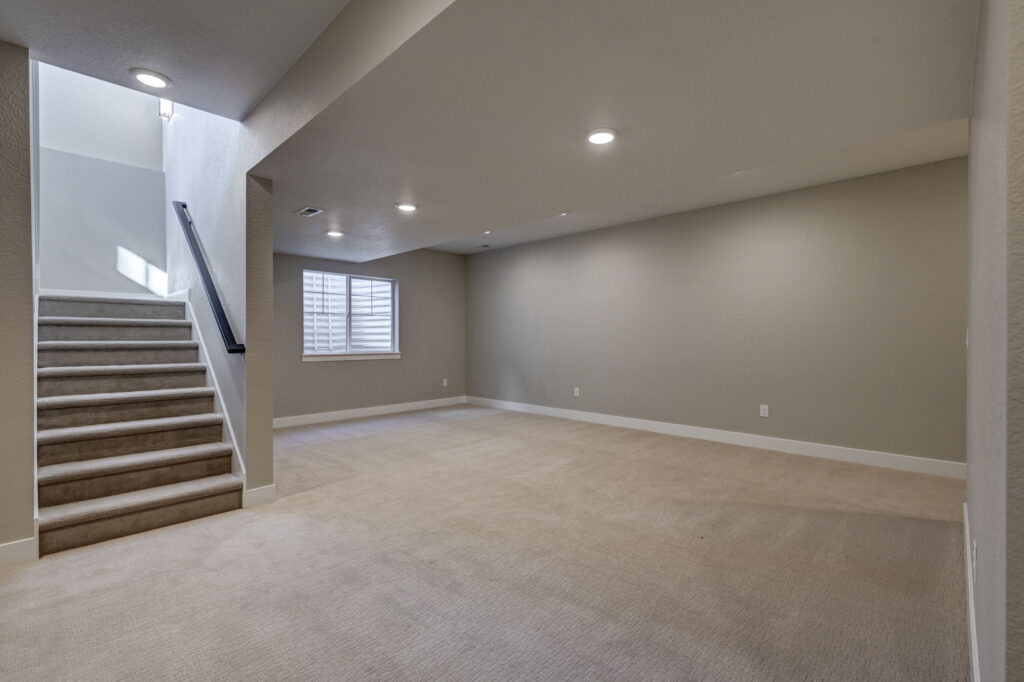 Carpeted finished basement room with recessed lights and stairs leading up at left.