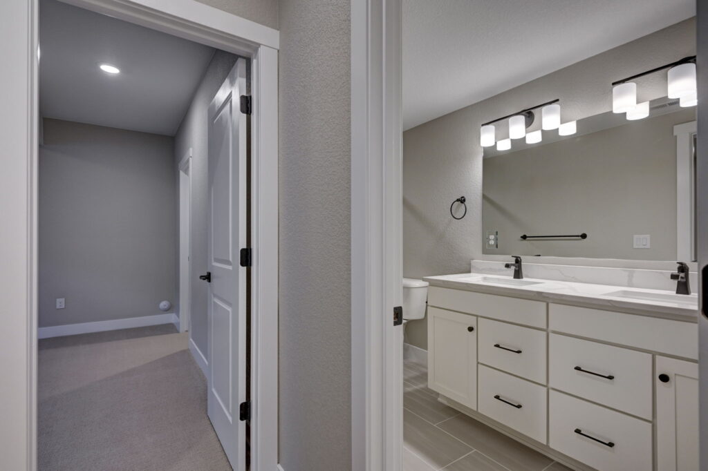 View into a hallway and an adjacent bathroom with double sink vanity and lit mirror.