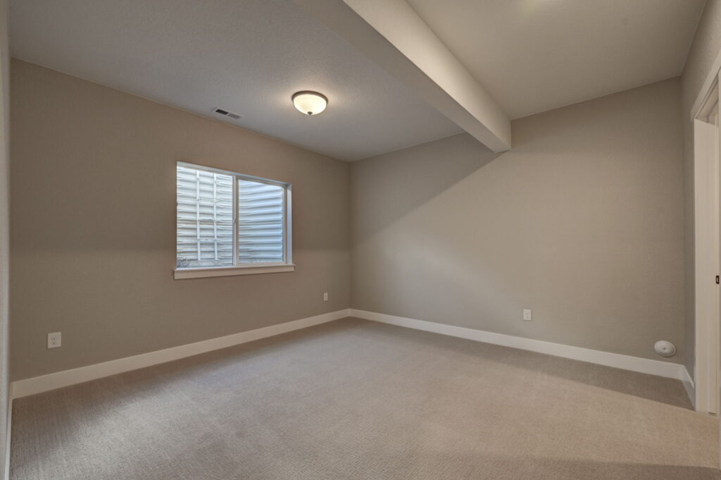 Empty room with carpet, window well, ceiling beam and soft neutral paint.