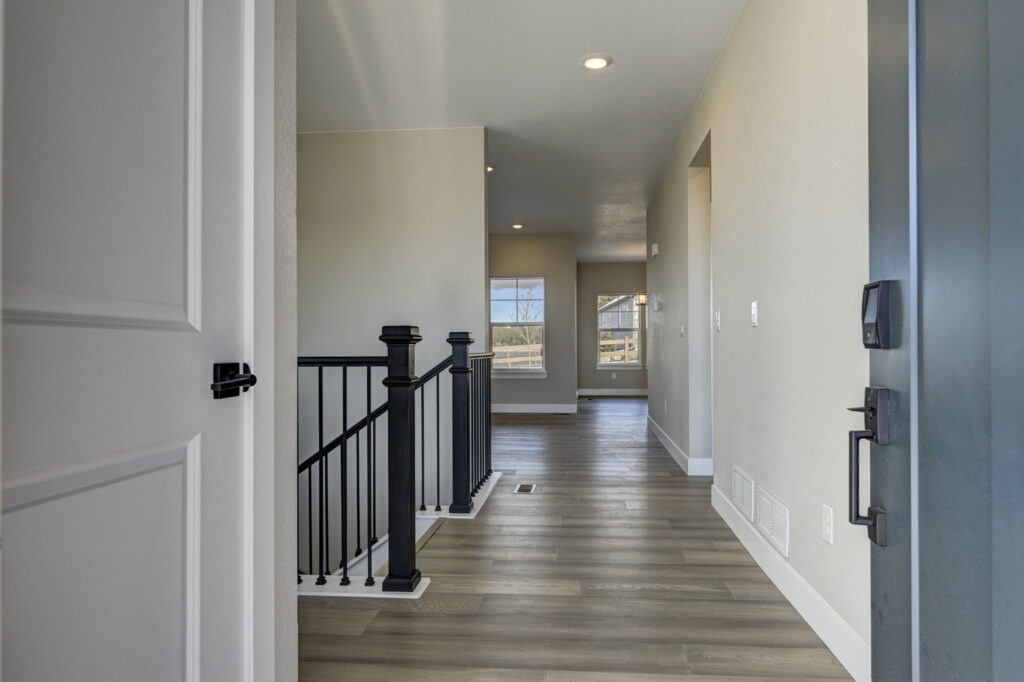 Hallway view from an entry with wood-look flooring, black stair railing, and windows ahead