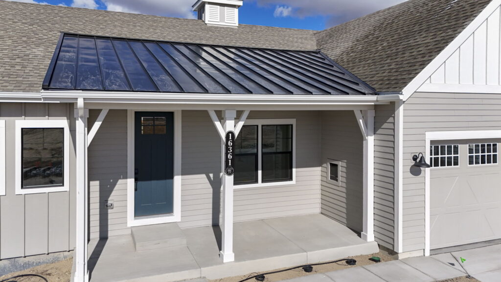 Covered front porch with blue entry door, white posts, address plaque, and metal roof overhang