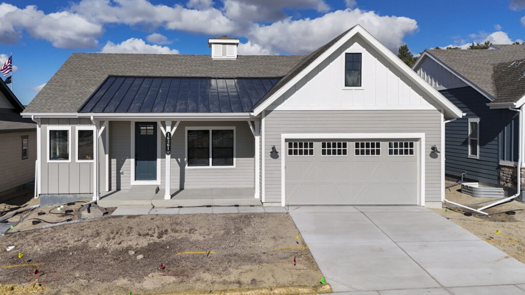 Single-story gray house with front porch, gabled roof and two-car garage under blue sky.