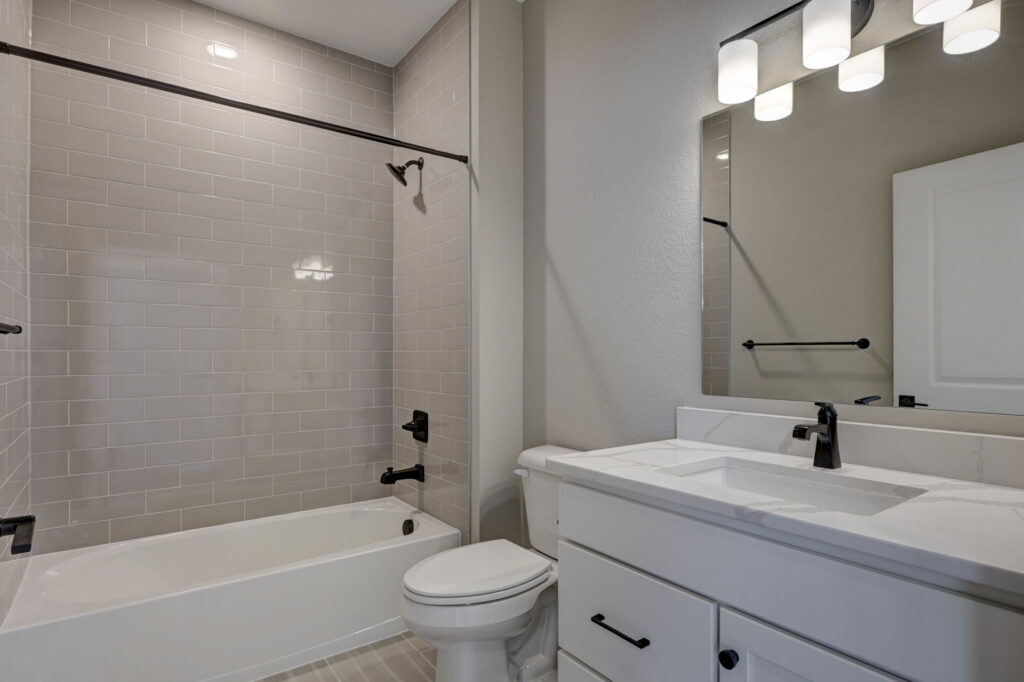 Bathroom with bathtub and shower tile, white vanity, mirror, and overhead light fixture.