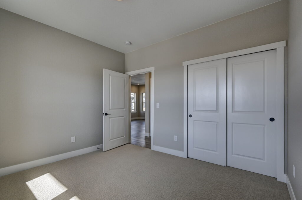 Empty bedroom with closed double-door closet and open door to hallway, neutral tones.