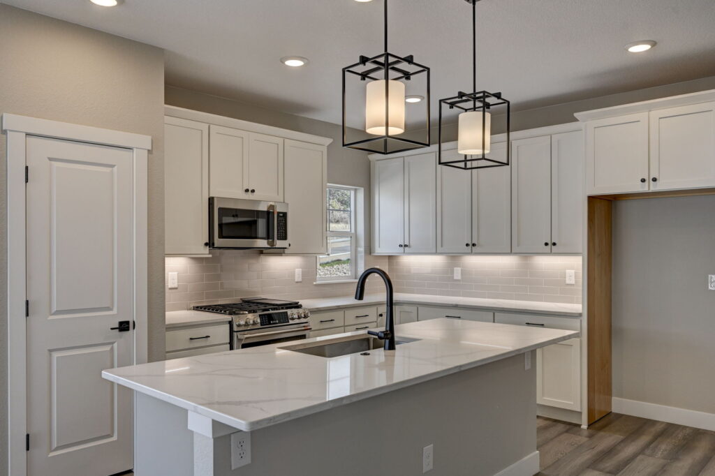 Close view of kitchen island with marble-look countertop, black faucet, and hanging lights.