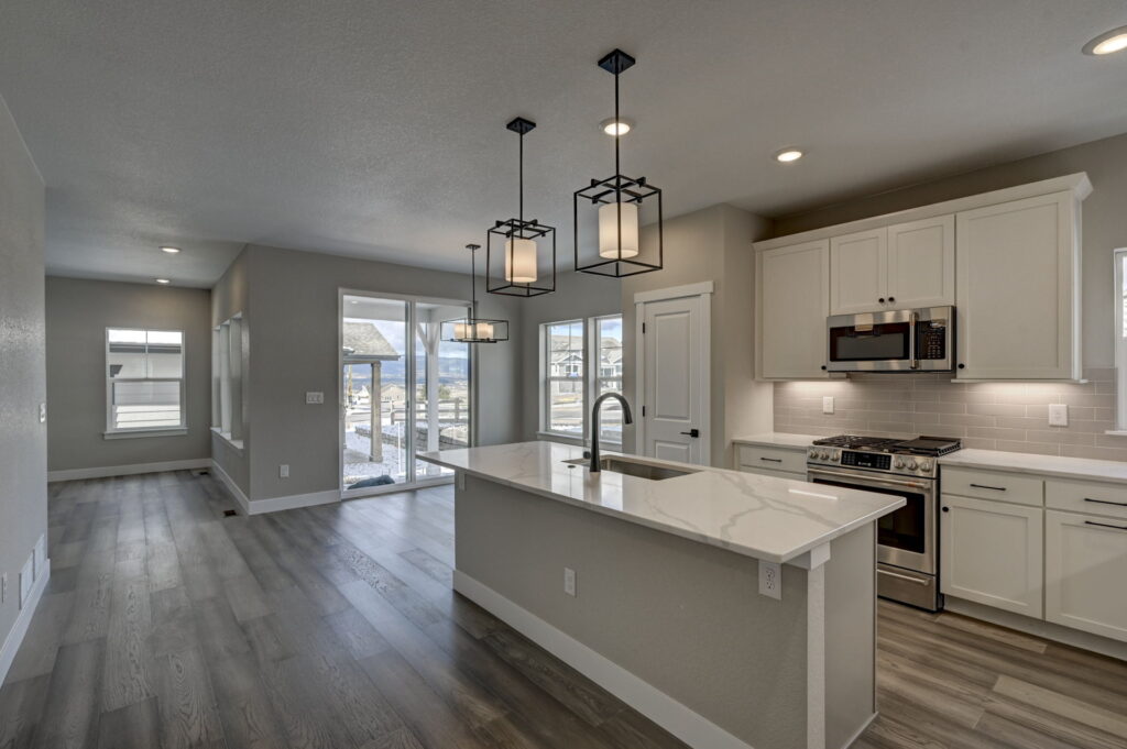 Wide-angle kitchen and dining area with island, pendant lights, and sliding doors to a patio.