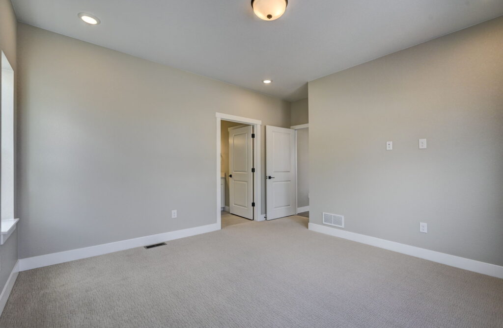 Empty room with open closet or bathroom door, neutral walls, and beige carpet.