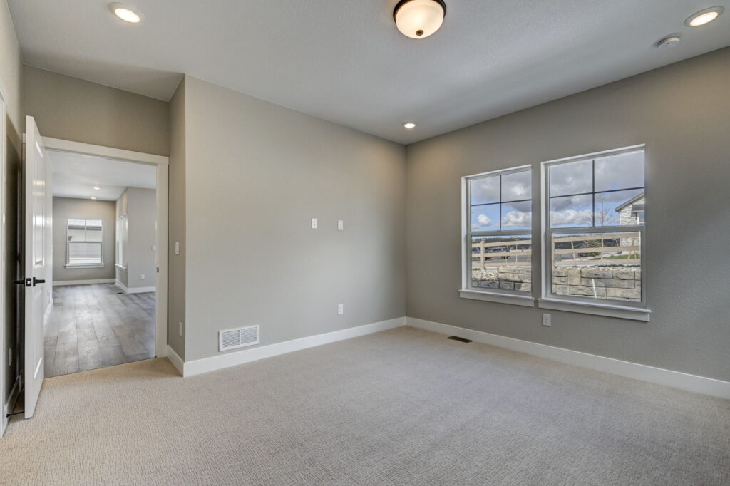 Empty carpeted room with two windows, gray walls, ceiling light, and open doorway to a hallway.