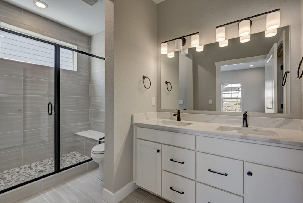 Bathroom vanity with dual sinks, large mirror, and a glass-enclosed tiled shower visible to the left.