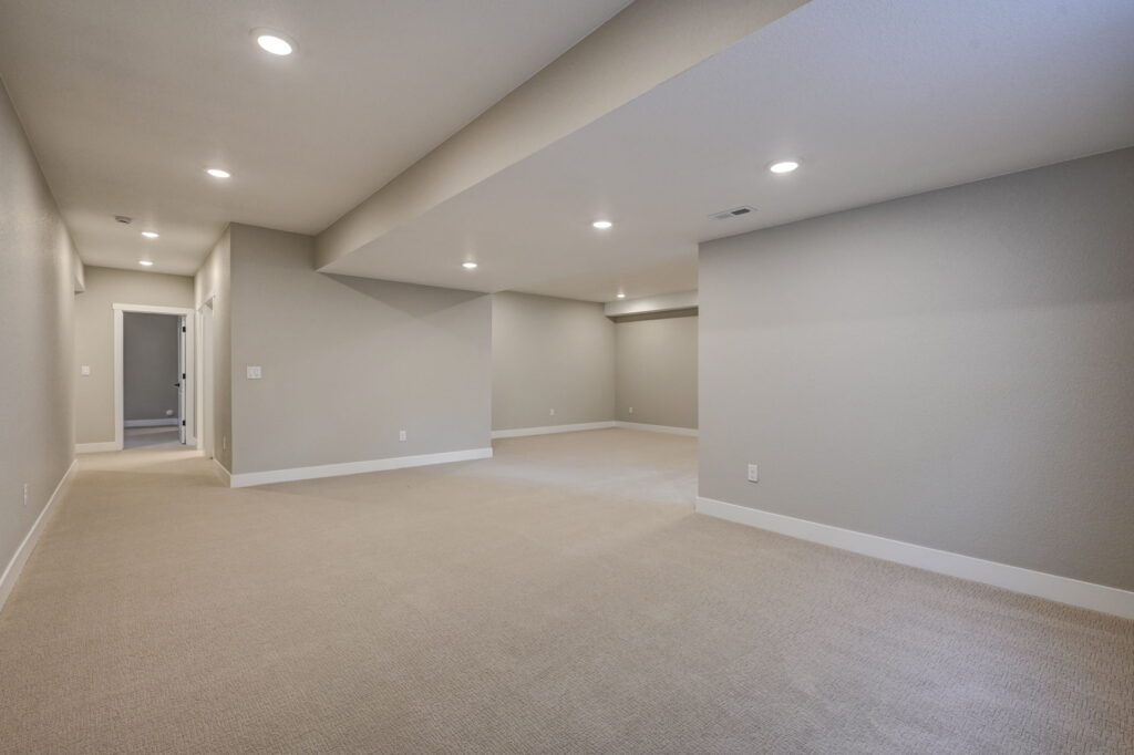 Long open basement area with a dropped ceiling beam and recessed lights.