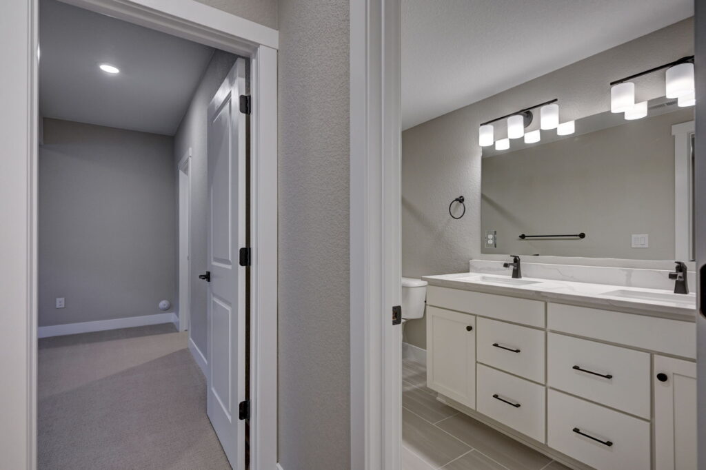 Bathroom vanity with double sink and a doorway to a carpeted hall.