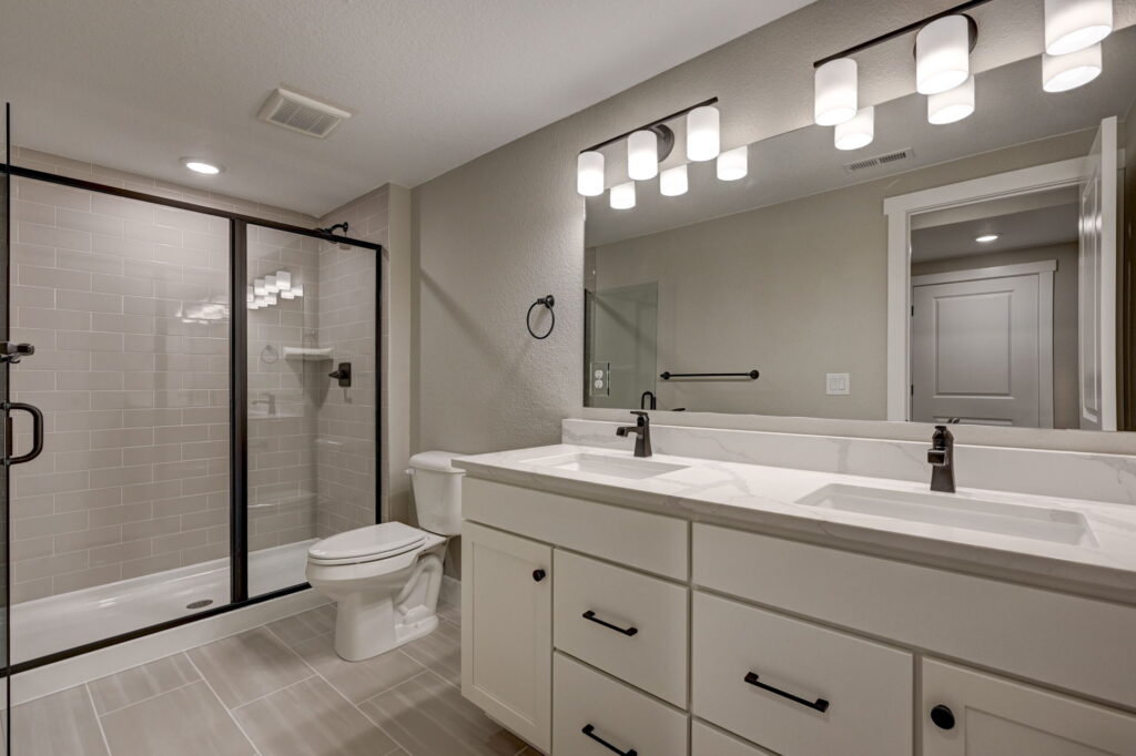 Modern bathroom with double-sink vanity, large mirror, toilet, and glass-enclosed shower.