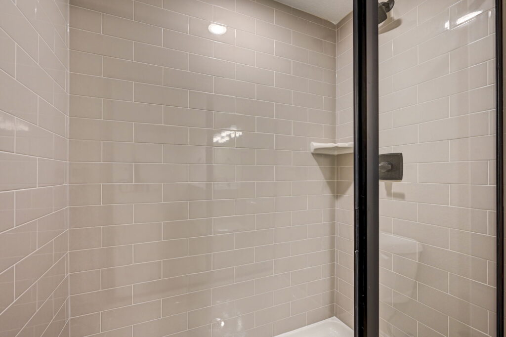 Close-up of a tiled shower with glossy subway tiles and a glass door frame.