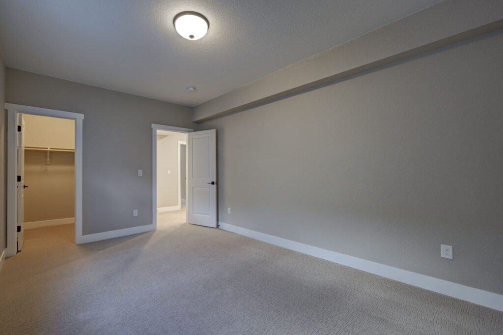 Unfurnished bedroom with open closet door, beige carpet and soft gray walls.
