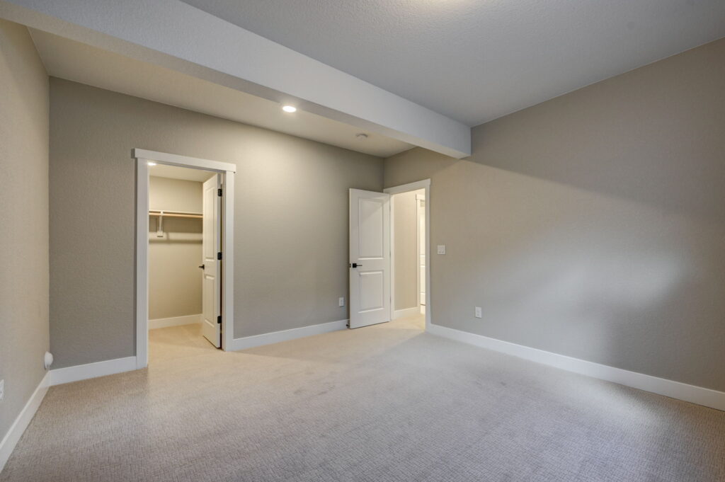 Carpeted bedroom with open closet and interior door, recessed ceiling light and beam.