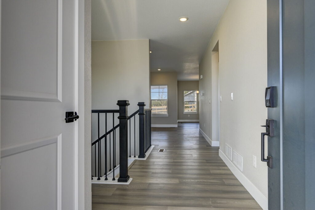 Entry hallway with wood-look flooring, black stair railing, and distant windows lighting the space.