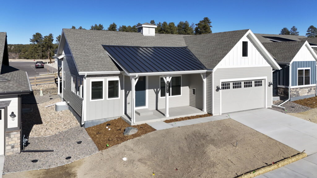 New single-story house with front porch, metal awning, attached garage, and bare front yard.
