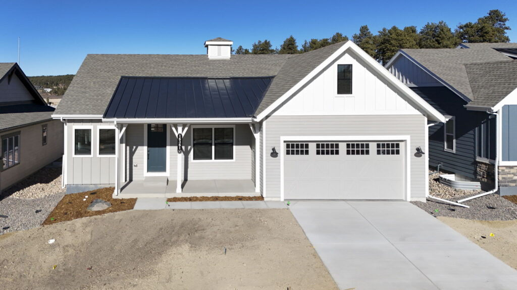 Single-story light-gray house with covered front porch and two-car garage under clear blue sky.