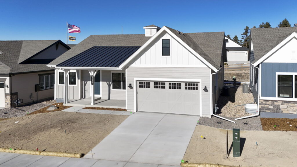 Similar front view of the same light-gray house showing adjacent homes and an American flag in the background.