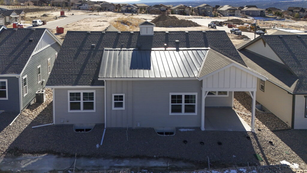 Rear exterior of a single-story house with metal roof panels and gravel yard.