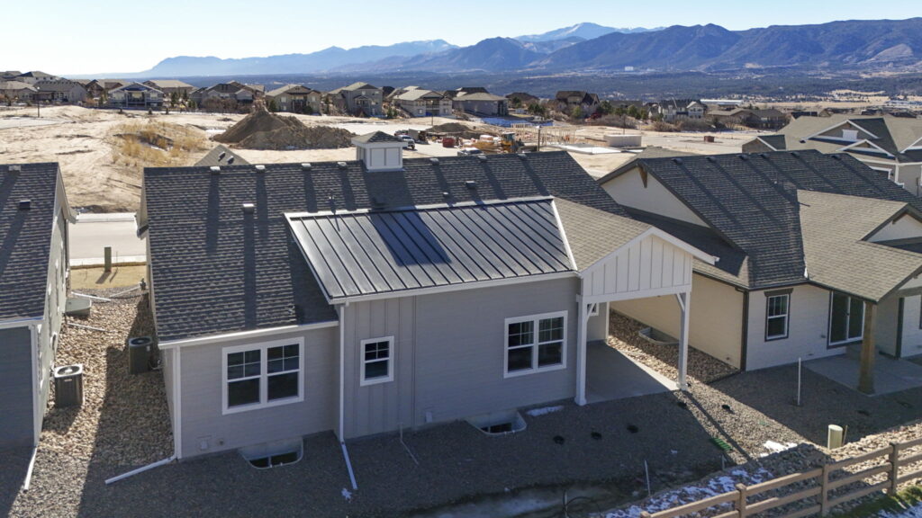Aerial rear view of a single-story home with metal roof section and neighborhood beyond.