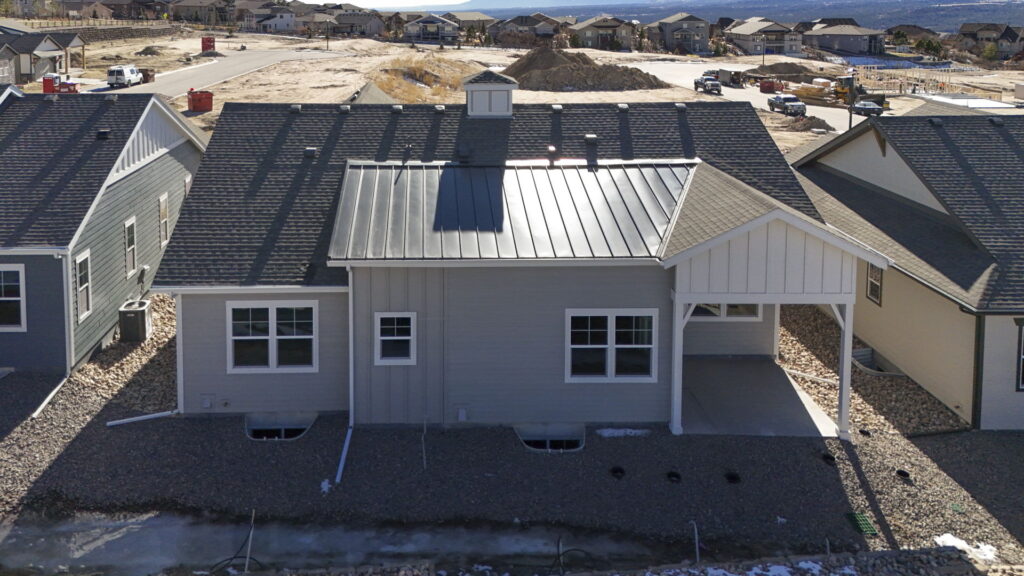Aerial rear view of a single-story home with metal roof section and adjacent houses.