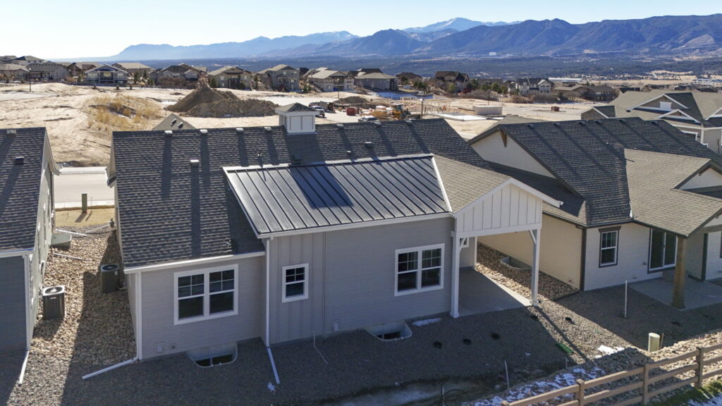 Aerial rear view of single-story house with metal roof accent and mountain backdrop.
