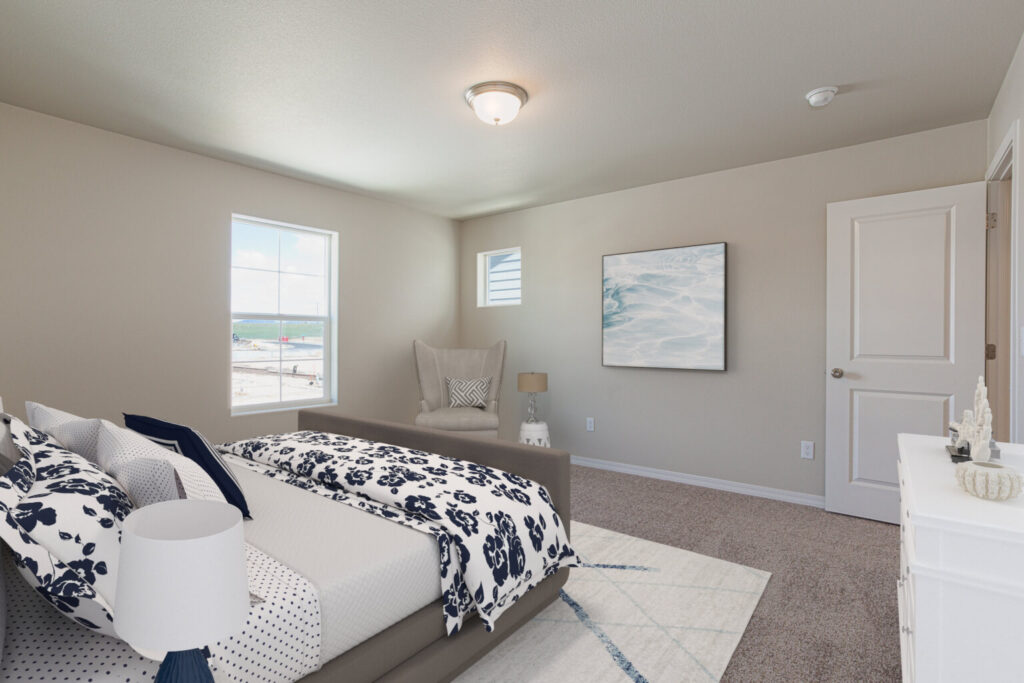 Bedroom view from foot of bed showing windows, armchair and dresser on carpeted floor.