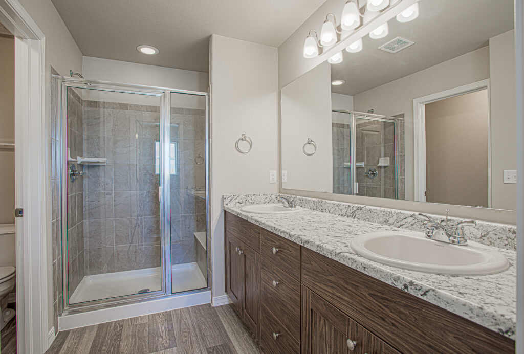 Bathroom with dual-sink vanity, granite countertop and glass-enclosed tiled shower.
