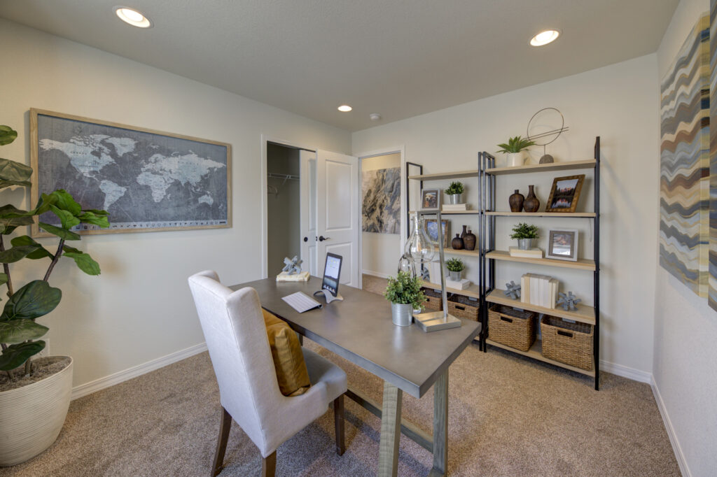Home office setup with desk, upholstered chair, shelving unit, map wall art, and recessed ceiling lights.