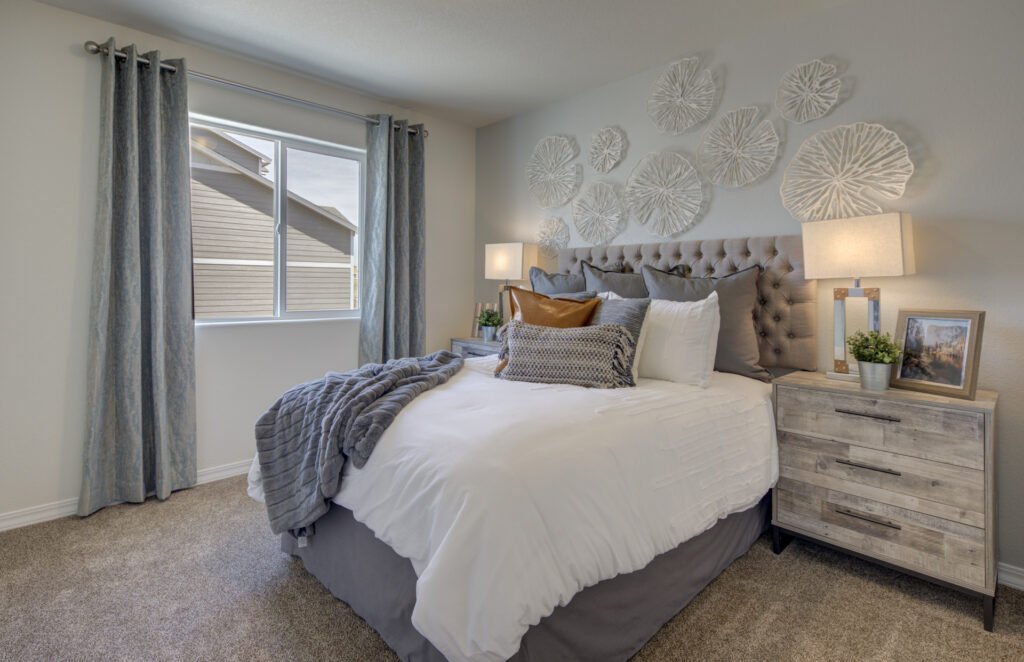 Well-lit bedroom with tufted headboard, textured wall art, and neutral bedding near a curtained window.