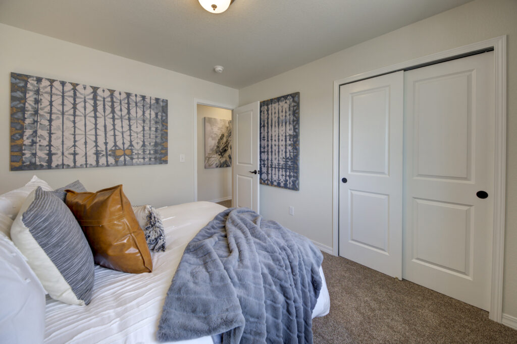Bedroom view showing bed with layered linens, closet with sliding doors, and framed wall art.