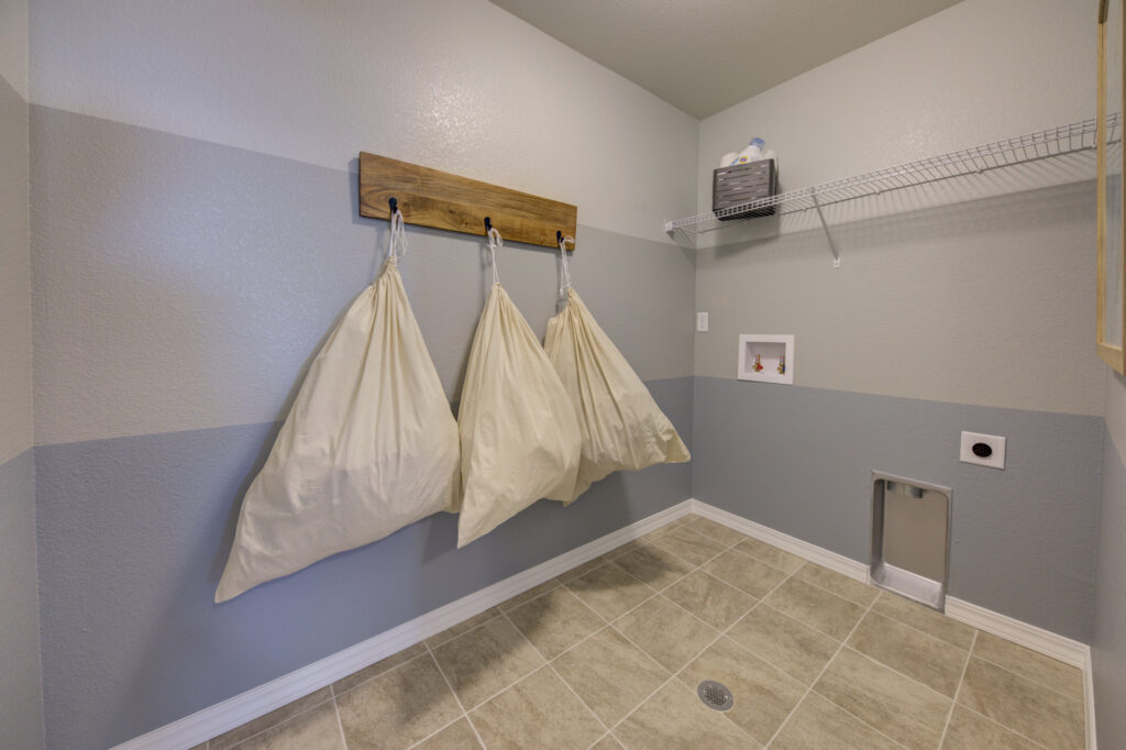 Laundry room with tiled floor, wall-mounted shelf, and three hanging fabric laundry bags on hooks.