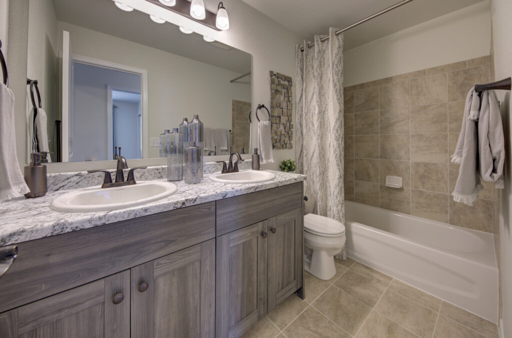 Bathroom with dual sinks, granite countertop, mirror, and a tub-shower with tiled surround and curtain.