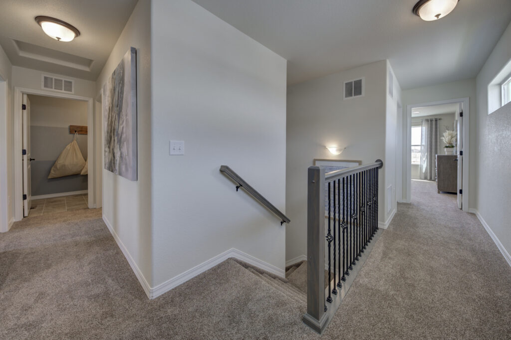 Carpeted upstairs landing with stair railing, hallway and open bedroom doors.