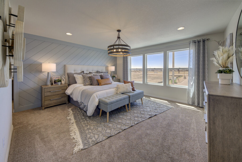 Bright bedroom with large windows, upholstered bed, patterned rug and round chandelier.