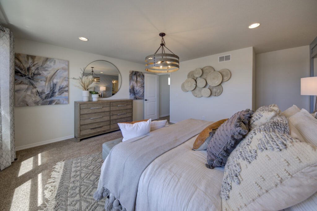 Close view from the bed of a decorated bedroom with dresser, round mirror and pendant light.