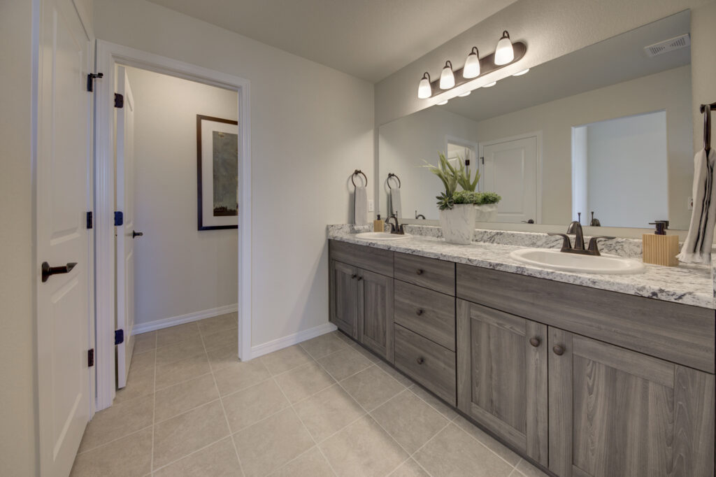Bathroom vanity with double sinks, marble-look countertop, gray wood cabinets and large mirror.