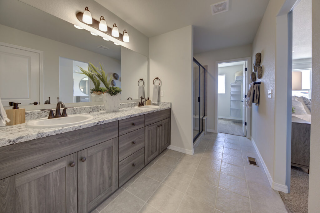 Wide view of a bathroom vanity and hallway to a shower and adjoining room with carpeted floor.