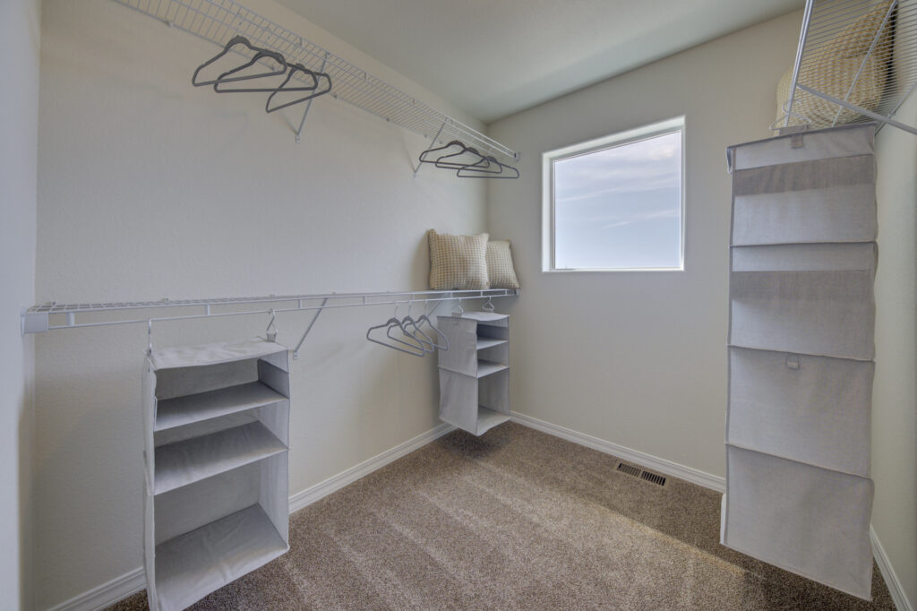 Walk-in closet with carpeted floor, wire shelving, hanging storage units, and a small window.