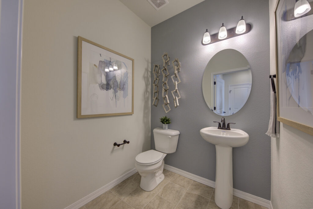 Small powder room with pedestal sink, oval mirror, toilet and framed wall art.