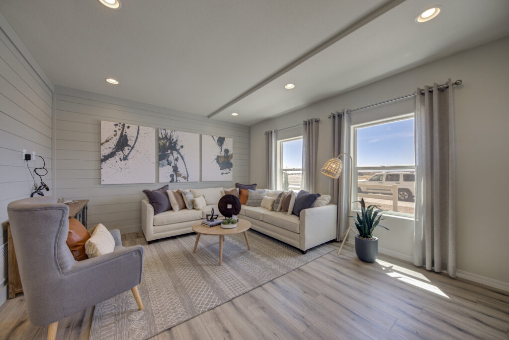 Bright living room with L‑shaped sofa, accent chair, and large windows letting in sunlight.