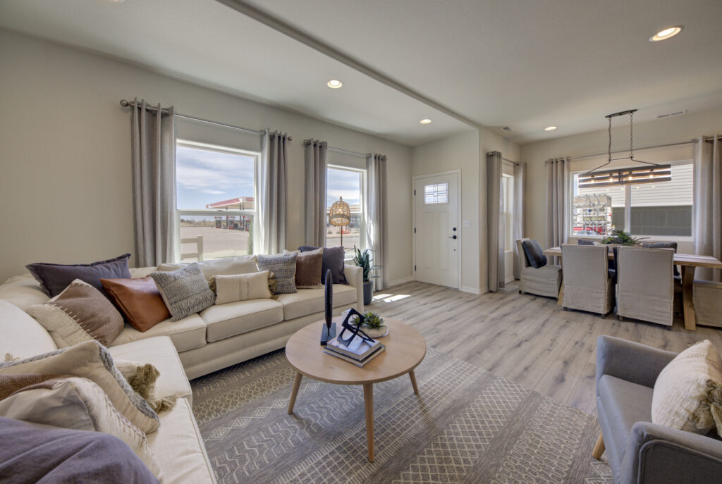 Open living and dining area with sofas, round coffee table, and dining table near front door and windows.