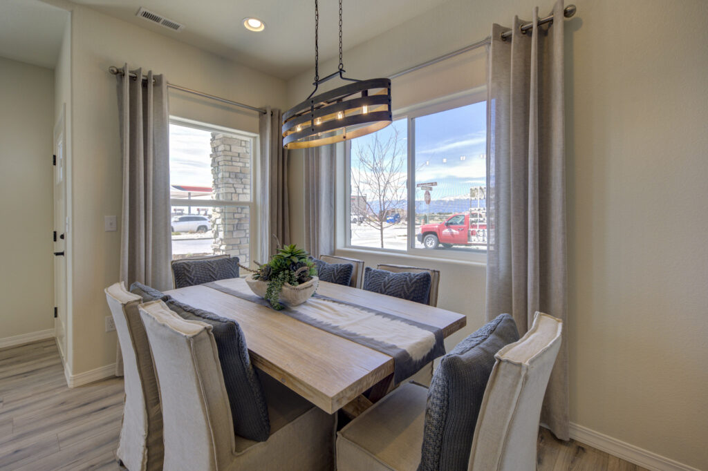 Dining nook with wooden table, six chairs, large window and modern chandelier.