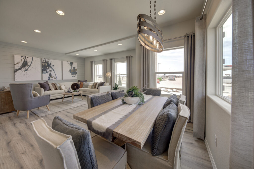 Open-plan dining and living area with wooden table, cushioned chairs, and sofa seating under pendant light.