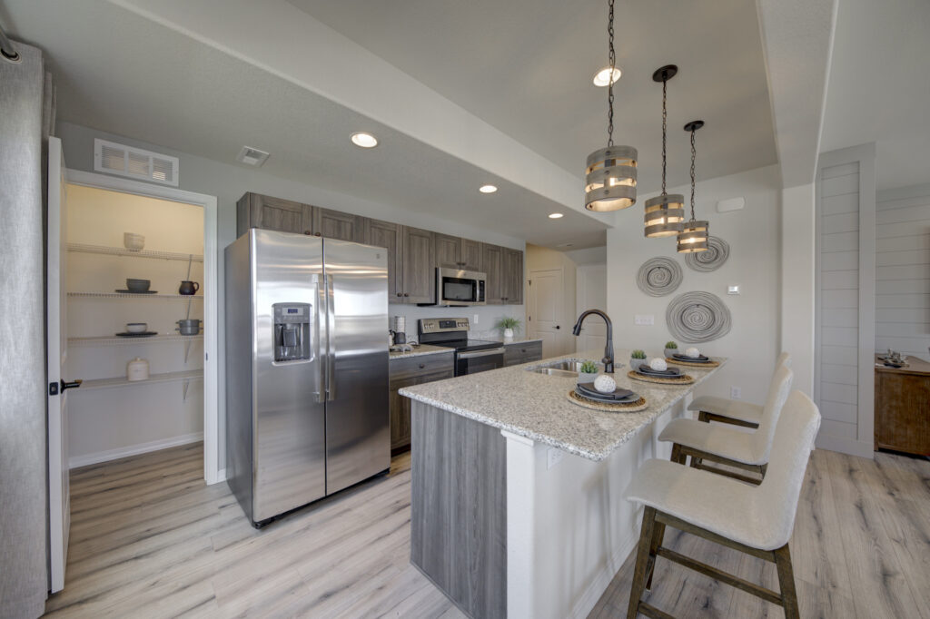 Kitchen island with three bar stools, stainless refrigerator, and open pantry door.