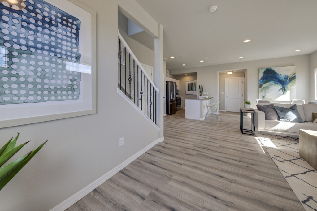 Open-plan living area with stairway, wood-look flooring, kitchen island and sofa.